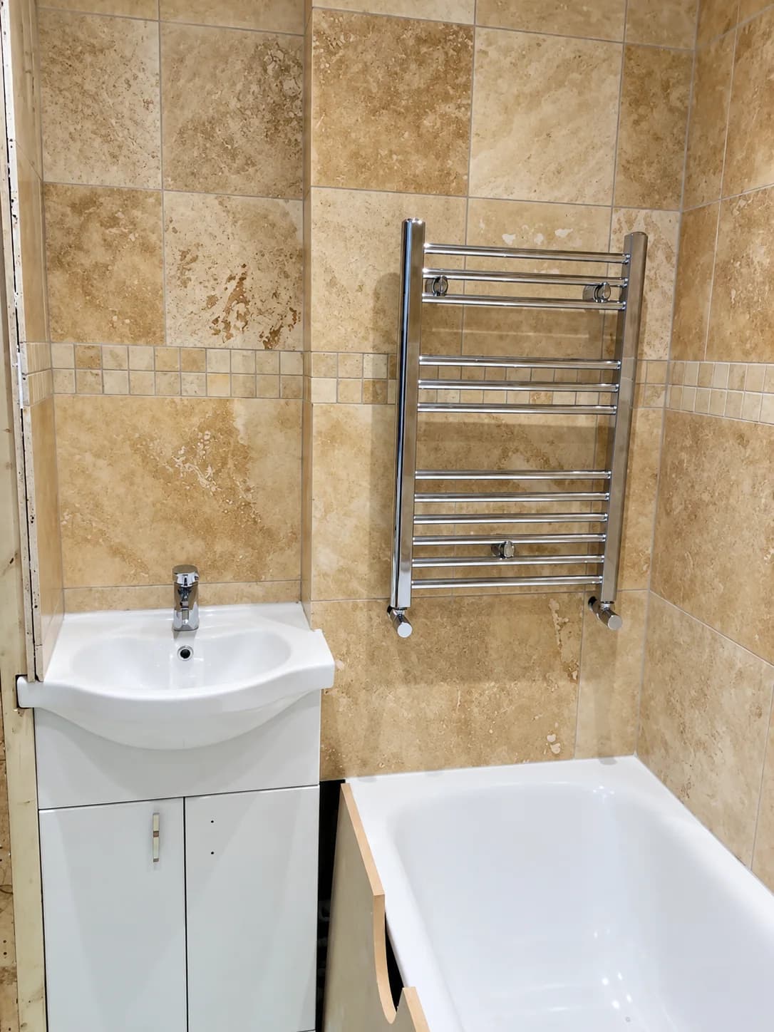 A tiled bathroom with a clean basin, chrome towel rail and bath fitted by CAF Heating